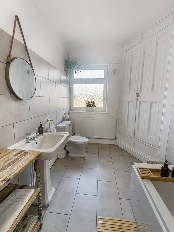 Bright bathroom with sink, toilet, bathtub, round mirror and window