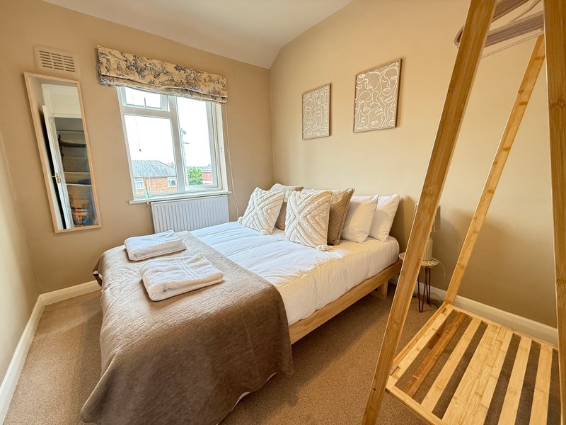 Bright bedroom with double bed, wooden four-poster frame, window with countryside view, and beige decor