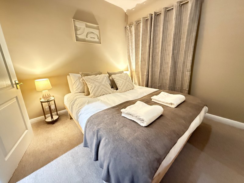 Modern bedroom with double bed, white pillows, grey bedding, bedside lamp and curtains