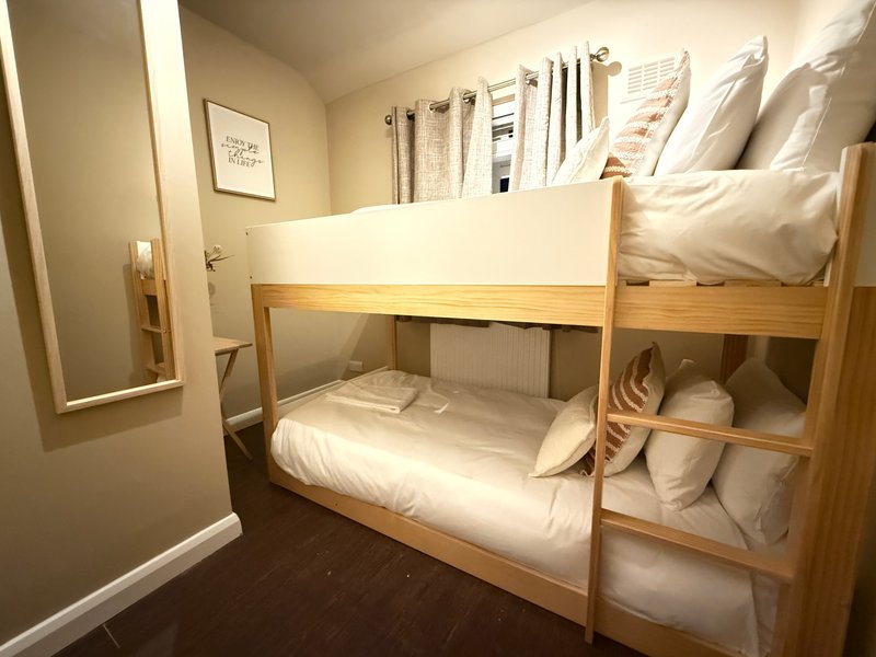 Compact bedroom with wooden bunk bed, white bedding, and small mirror on wall