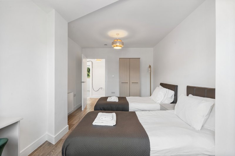 Bright bedroom with two single beds, wooden floor, and ensuite bathroom visible
