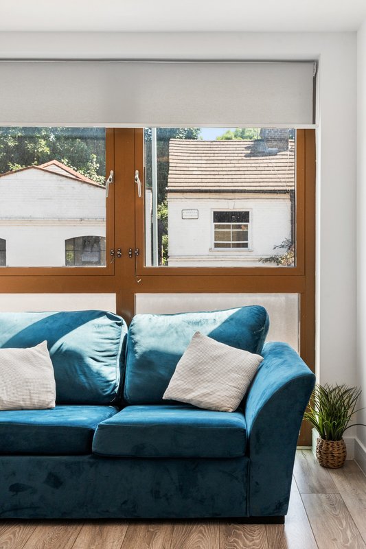 Blue upholstered sofa with cushions facing large wooden-framed windows overlooking residential buildings