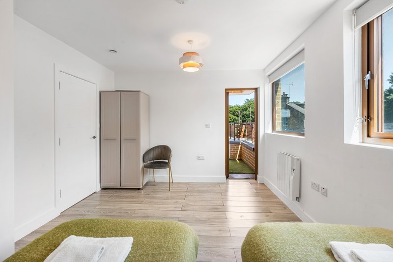 Bright modern living room with green upholstered seating, wooden flooring, and glass door to balcony