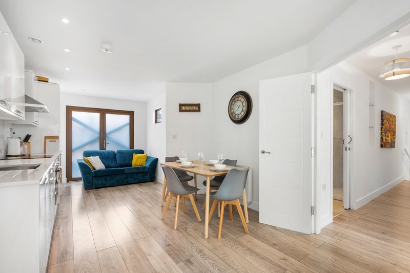 Open-plan living space with blue sofa, dining table, kitchen area and sea view through glass doors