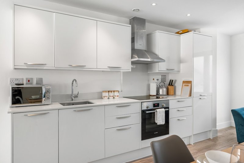 Modern white kitchen with integrated appliances, stainless steel cooker hood and wooden flooring