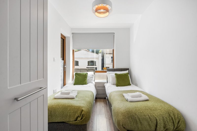 Compact bedroom with two single beds, green bedding, white walls and ceiling light