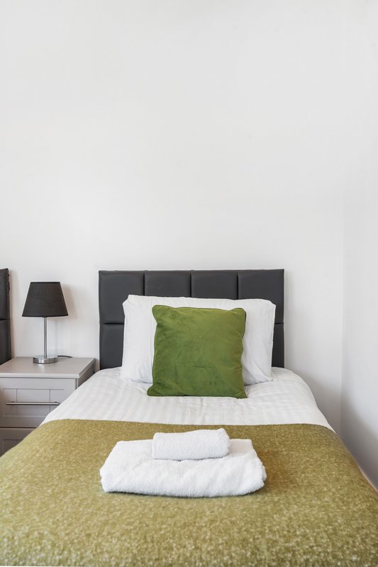 Bedroom with double bed, dark headboard, green cushion and bedding, white pillows and towels