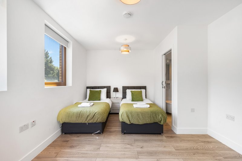 Twin bedroom with two single beds, green bedding, wooden floor and window