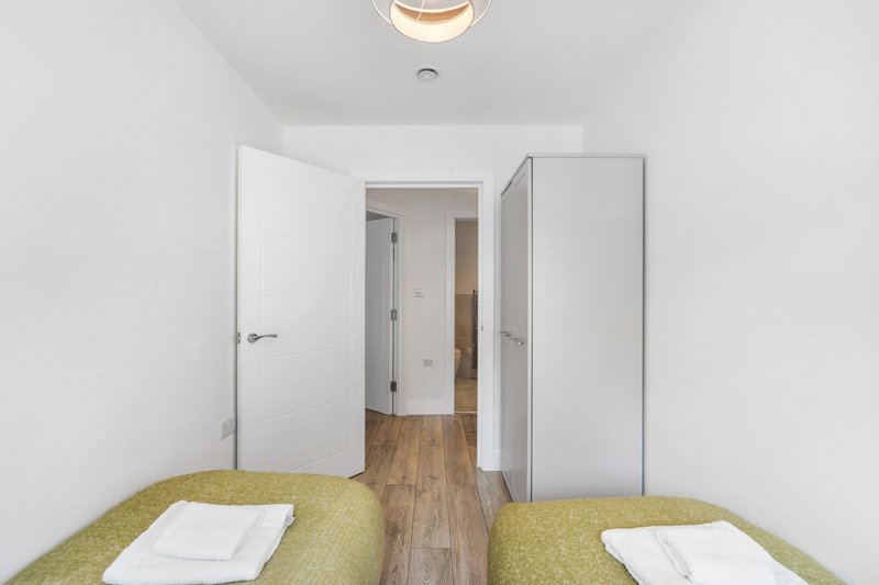 Bright twin bedroom with yellow-green bedspreads, white doors, wooden floor and hallway view