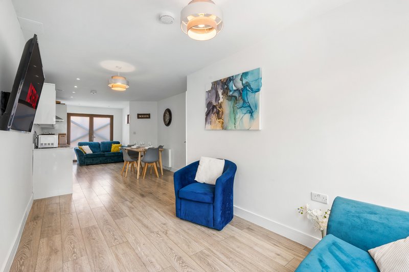 Open-plan living area with blue armchair, wooden flooring, kitchen, and wall art
