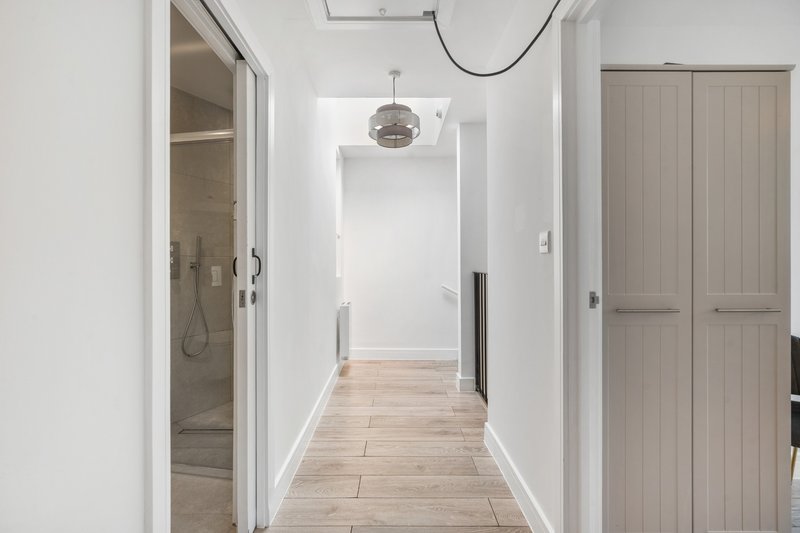 Bright hallway with wooden flooring, white walls, pendant light, and open doorways