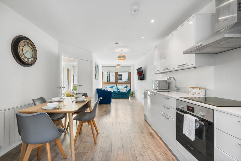 Modern open-plan kitchen and dining area with white cabinetry, wooden table, and living room visible beyond