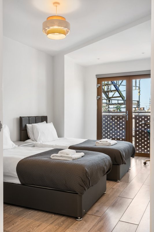 Bright bedroom with two single beds, dark upholstered headboards, wooden floor and pendant light