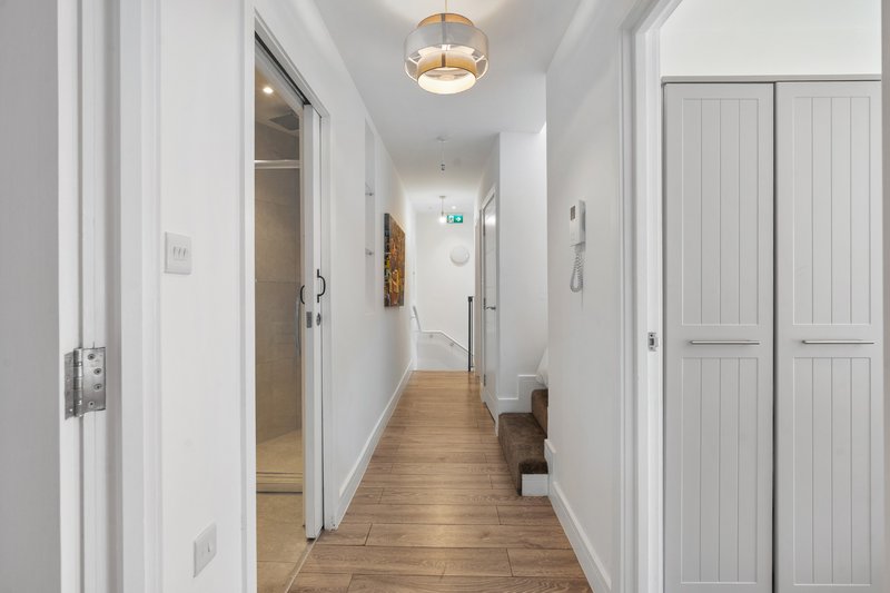 Bright hallway with wooden floor, white walls, doors and ceiling pendant light