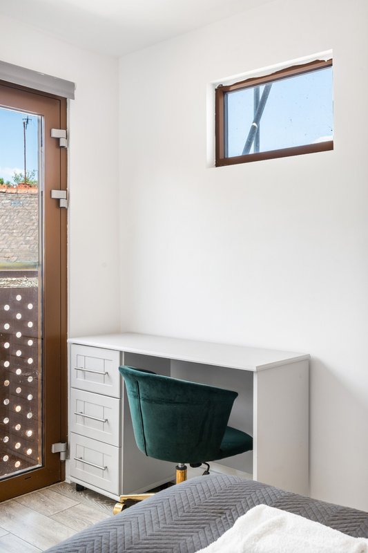 Bright bedroom corner with white storage unit, green chair, wooden door and window