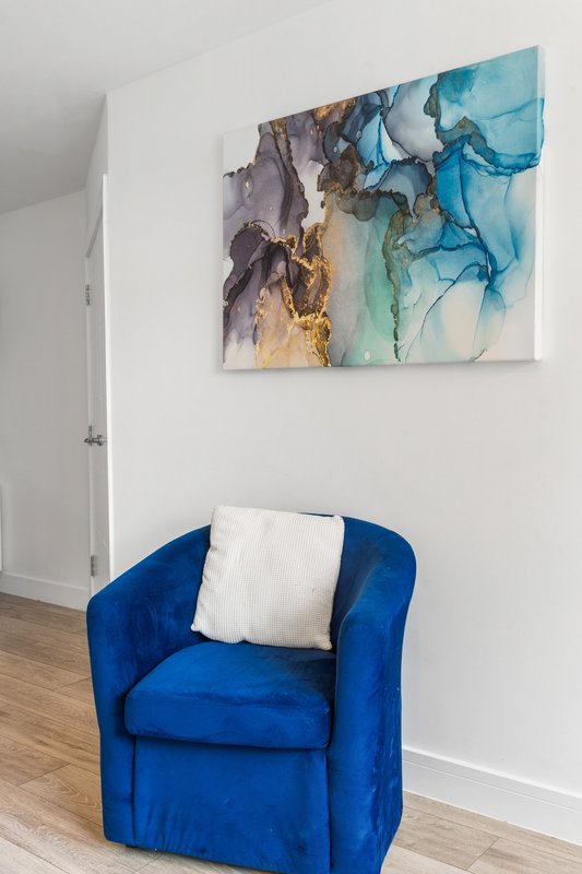 Modern interior with blue upholstered armchair, white cushion, and abstract wall art
