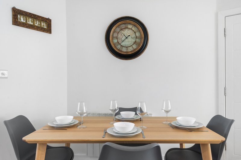 Wooden dining table set for four with black chairs, wall clock and decorative sign above