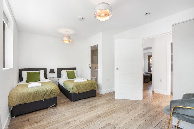 Modern bedroom with two single beds, wooden flooring, pendant lights and white walls