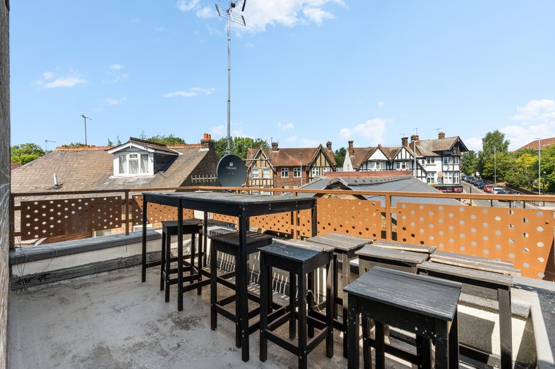 Rooftop terrace with high-top seating, orange privacy screen, and townhouse roofline views