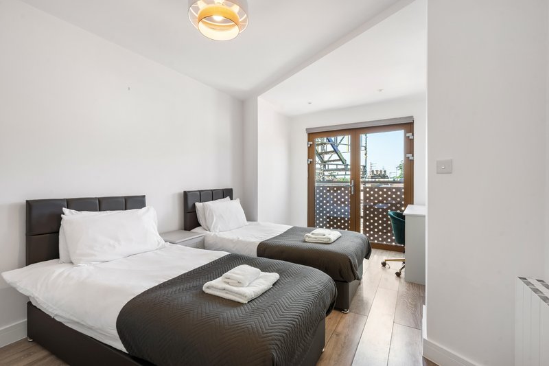 Bright bedroom with two single beds, dark headboards, white bedding and wooden flooring