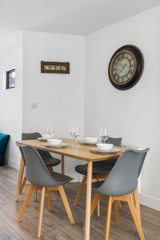 Dining area with wooden table, grey chairs, wall clock and place settings