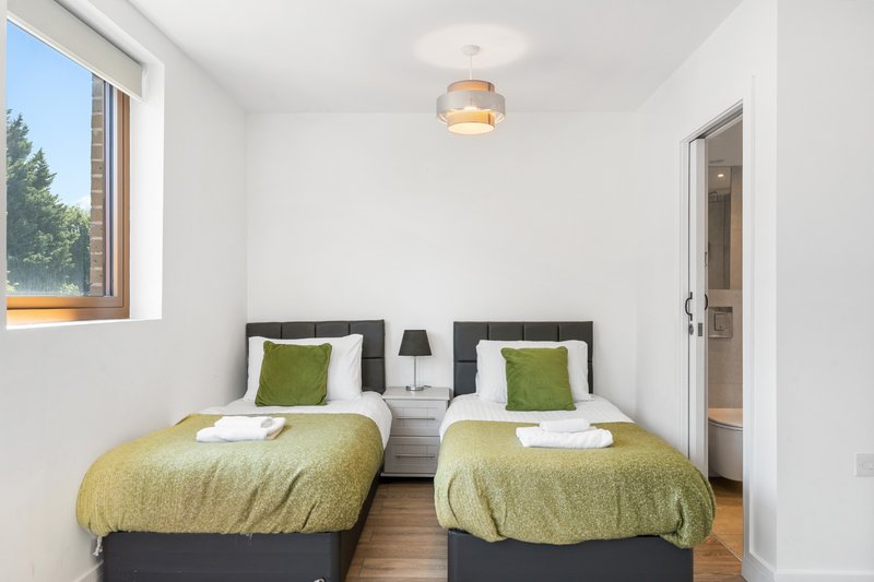 Twin bedroom with two single beds, green bedding, green pillows, wooden floor and window