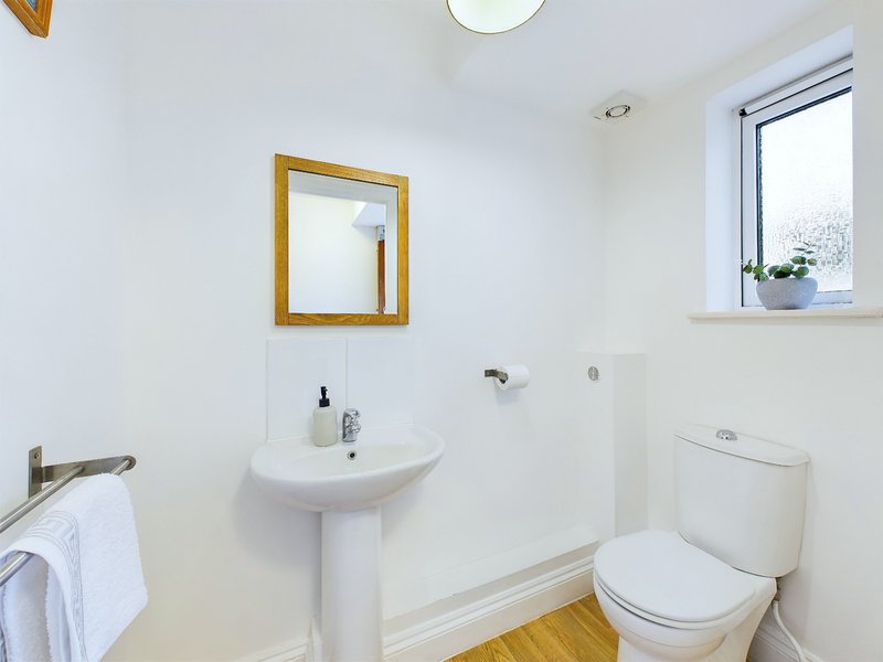 Clean bathroom with pedestal sink, toilet, mirror and small window
