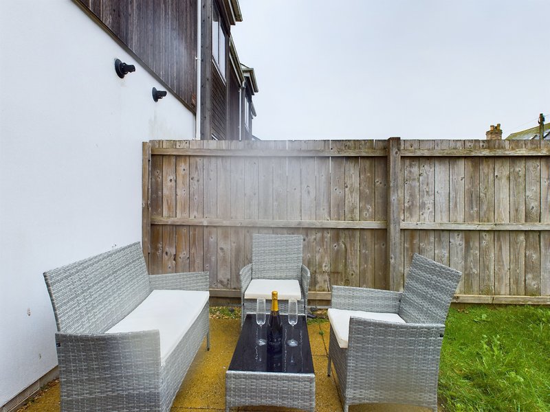 Outdoor patio seating area with woven chairs, bench seating, and fire table on decking