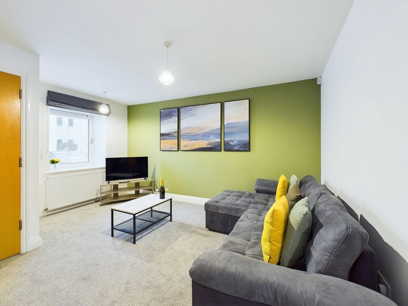 Modern living room with grey sofa, yellow cushions, TV, and green accent wall