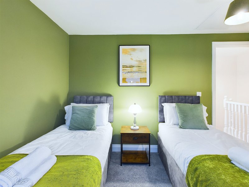 Twin bedroom with green walls, two single beds, bedside table and framed wall art