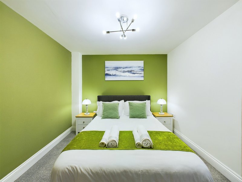 Modern bedroom with lime-green walls, double bed, white nightstands, and landscape artwork above headboard