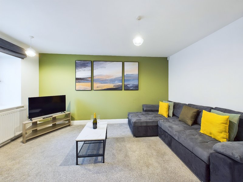 Modern living room with gray sectional sofa, yellow accent pillows, TV stand, and landscape artwork