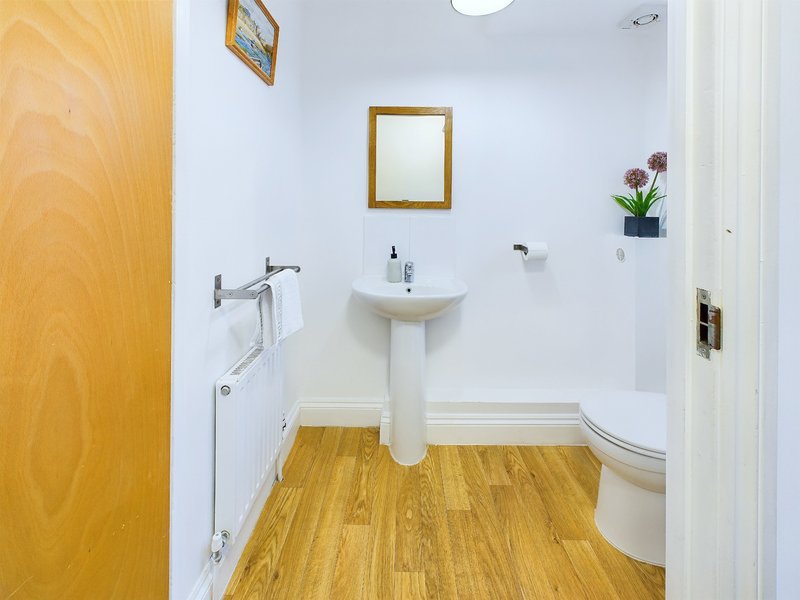 Clean bathroom with pedestal sink, wooden floor, framed mirror and potted flowers