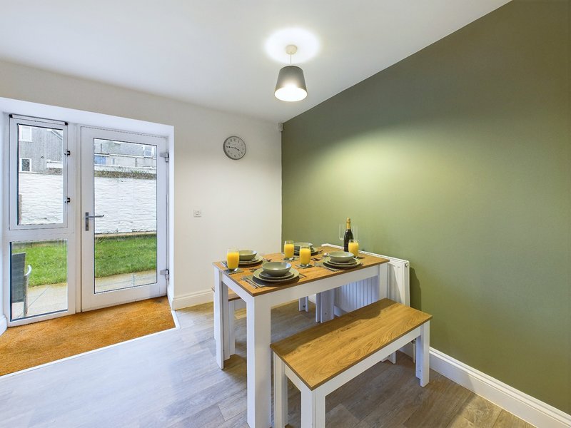 Dining area with white table, wooden bench seating, green accent wall and glass doors to garden