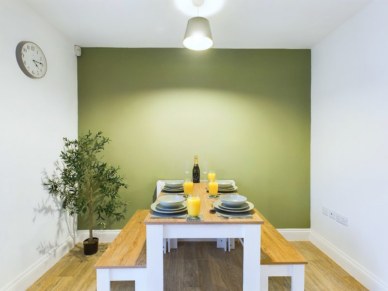 Modern dining nook with wooden table, bench seating, green accent wall and table setting