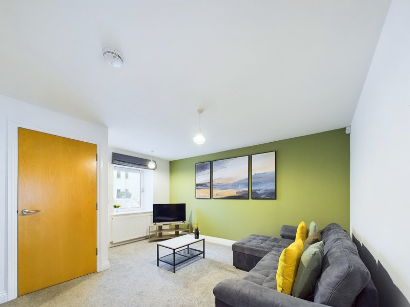 Bright living room with green accent wall, gray sofa, yellow door, and window views