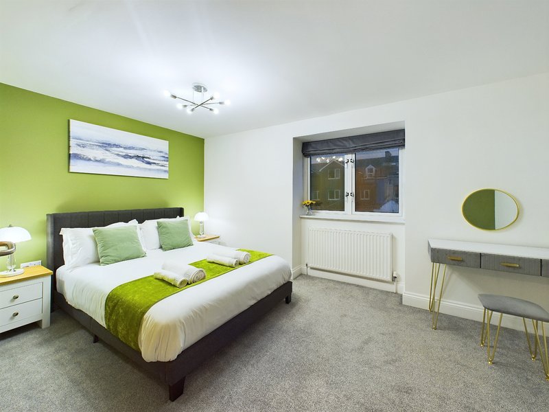Modern bedroom with lime green accent wall, double bed with white bedding and green throw, desk and mirror