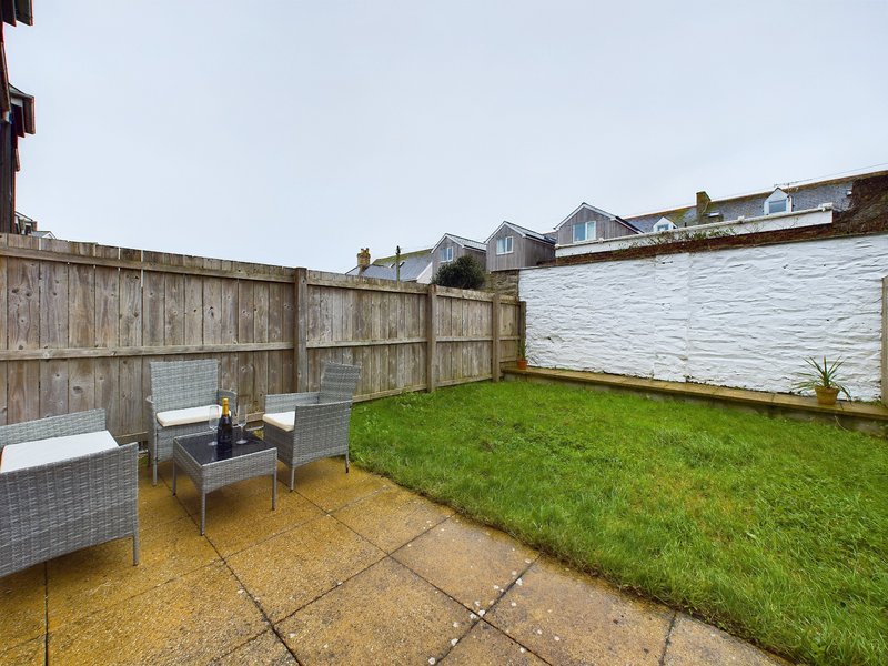 Enclosed garden with patio seating area, green lawn, wooden fencing and neighboring properties