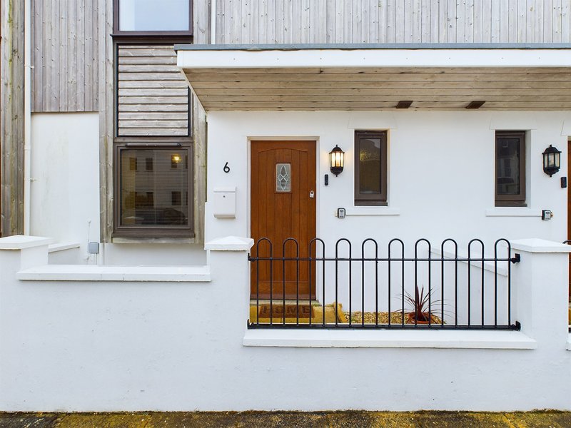 Modern white property exterior with wooden door, metal railings and decorative planters
