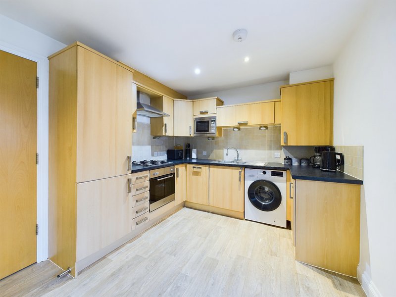 Modern kitchen with yellow wooden cabinets, integrated appliances, black countertops and light flooring