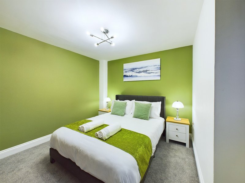 Bright green bedroom with double bed, white bedding, green throws and matching wall art