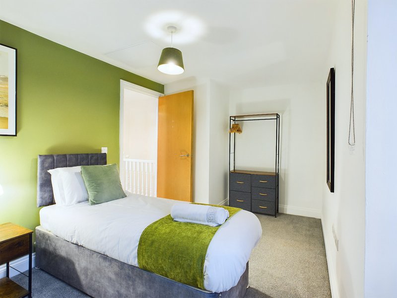 Bedroom with double bed, green accent wall, wooden door, and chest of drawers