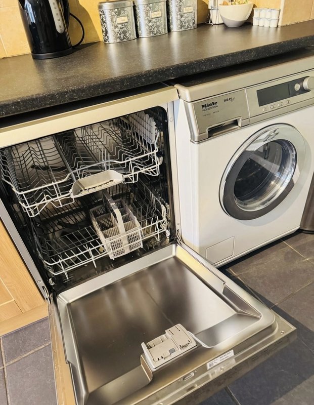 Kitchen countertop with open dishwasher, washing machine, and countertop appliances