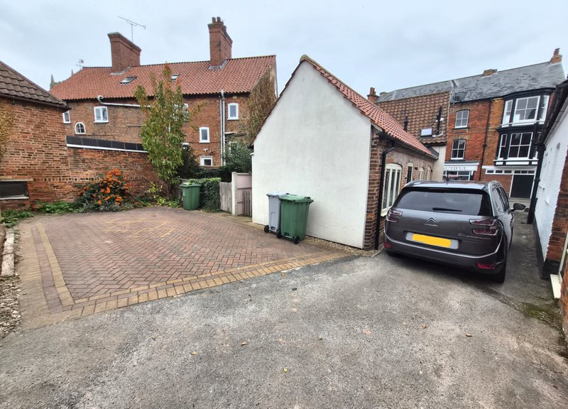 Brick driveway with parked car, white cottage, and brick residential buildings