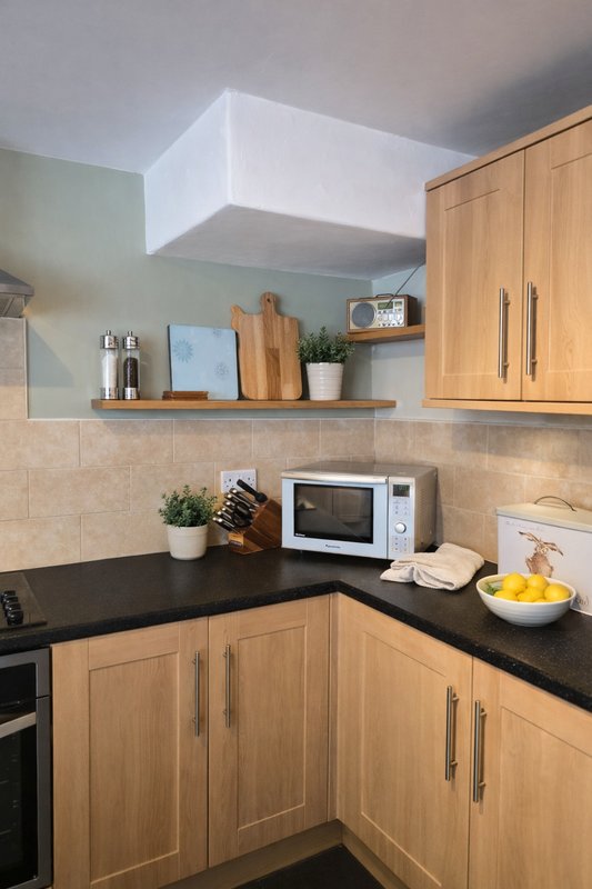 Modern kitchen with wooden cabinets, black countertop, white microwave and open shelving