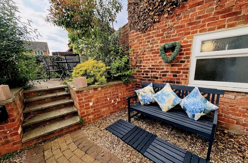 Brick patio with black bench, cushions, steps, and climbing ivy decoration