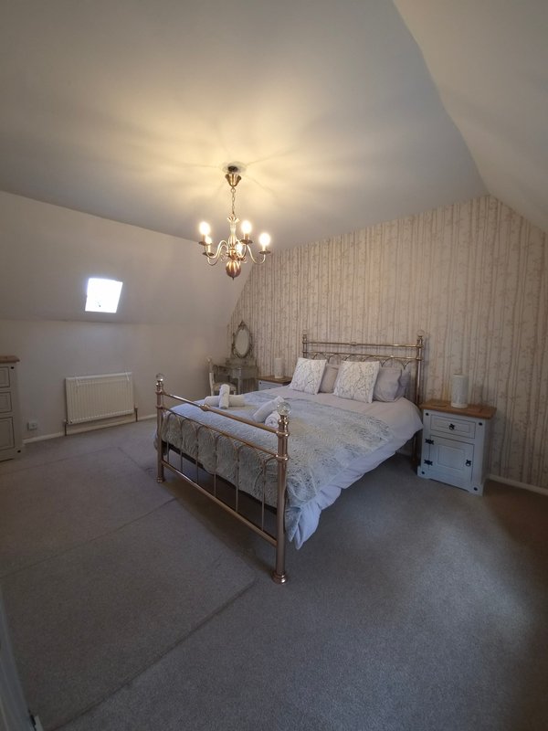Attic bedroom with metal bed frame, striped wallpaper, chandelier, and white nightstand