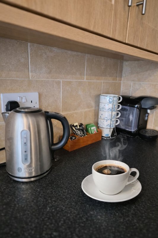 Kitchen counter with kettle, coffee cup, and appliances on black worktop