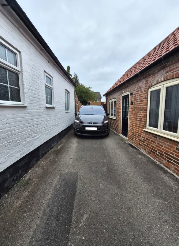 Driveway between white and brick houses with parked car