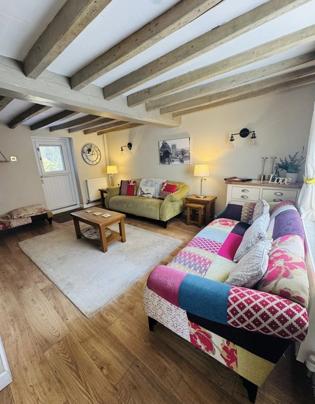 Spacious open-plan bedroom with exposed beams, sofa, bed with colorful patchwork quilt, and wooden furniture.